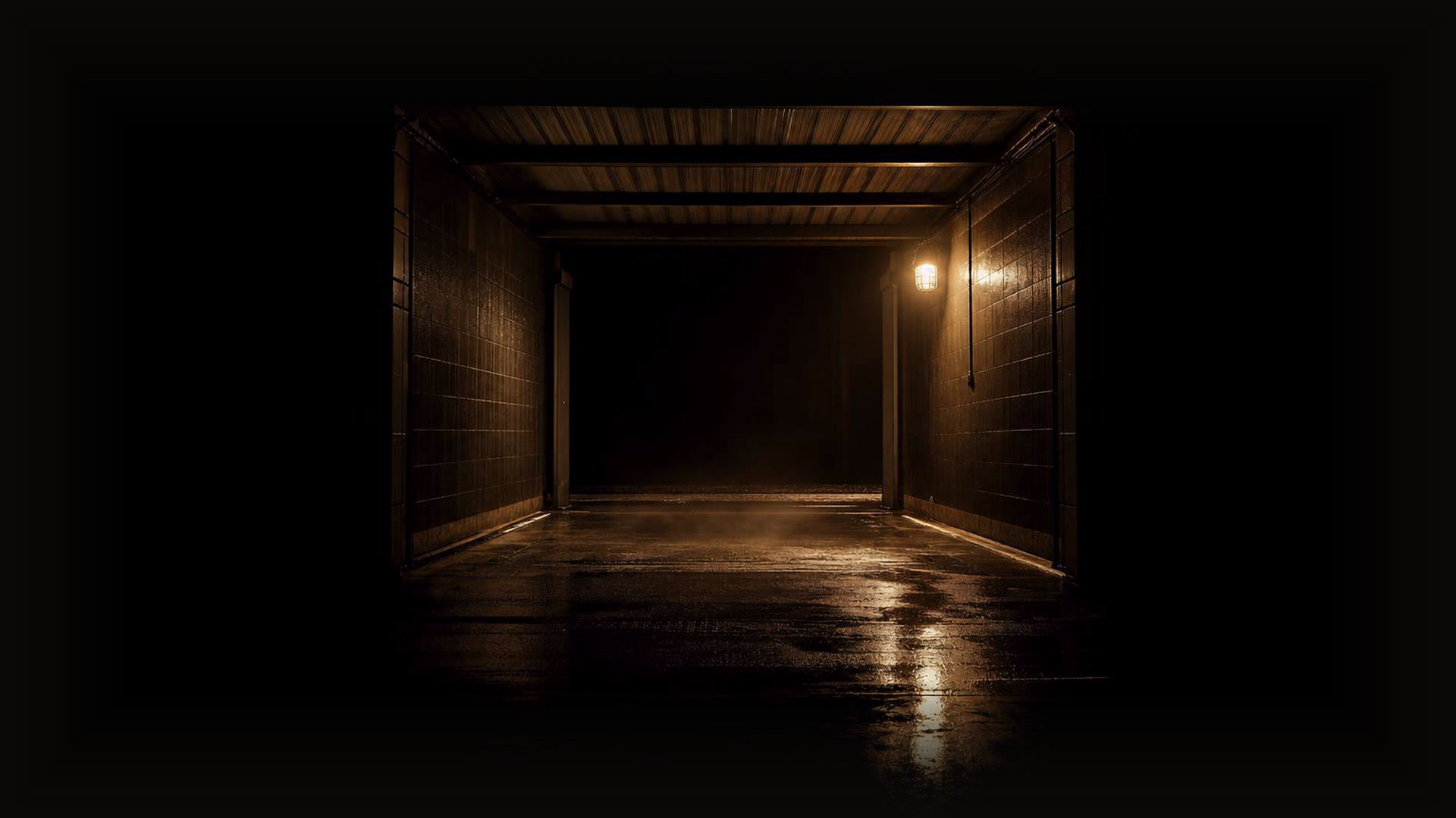 The empty wash bay at dusk, wet floor shining under one warm caged lamp, dissolving into darkness
