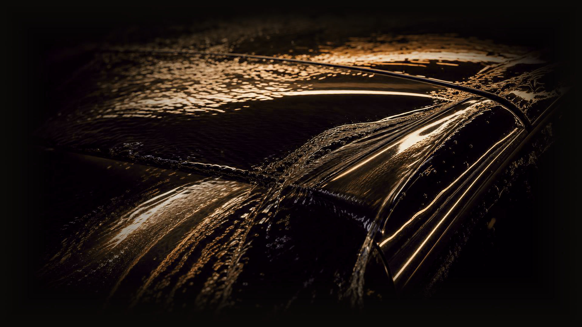 Water sheeting across dark glossy paint, catching warm light, dissolving into darkness at the edges