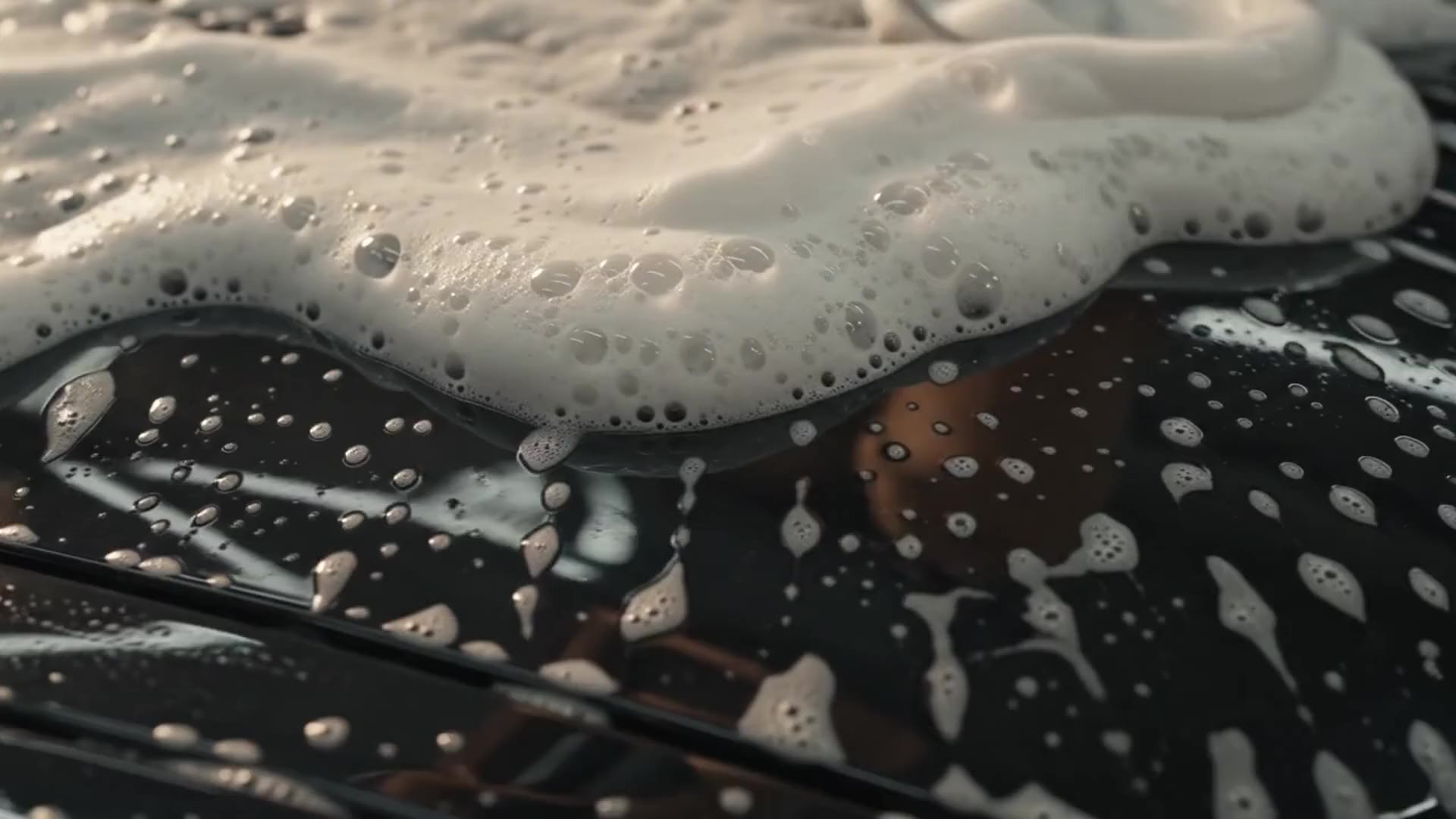 Thick foam rolls slowly down dark paint in heavy sheets